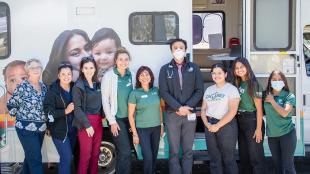 Nine people stand, some wearing masks, smile in front of Cal Poly's Mobile Health Unit