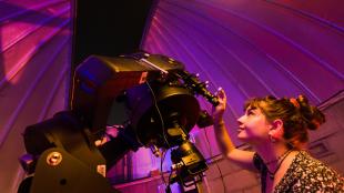 A student uses a large black telescope in an on campus observatory