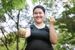 A woman in a black shirt exercises while smiling and holding an apple