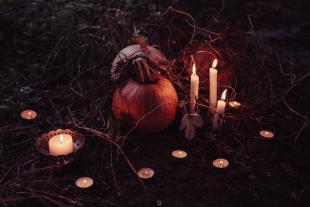 Small lit candles and branches surround two pumpkins. 