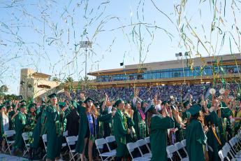 Graduating students stand and cheer as streamers float above their heads at Spanos Stadium during Cal Poly's spring 2019 commencement.