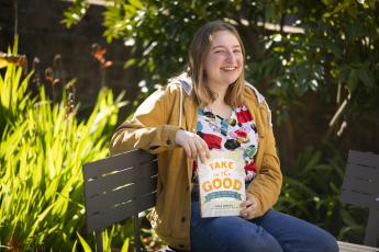 Breanna Chambers holds her book, "Take in the Good" as she sits on a bench next to the Dexter building at Cal Poly.