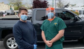 Alan Puccinelli, left, and a medical doctor, right, wear face shields and pose in front of a truck.