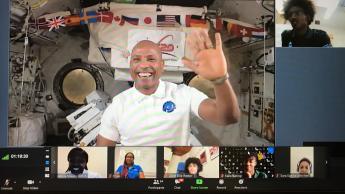 Victor Glover waves on a screenshot of a Zoom call with a space shuttle background. Seven smaller screens show students. 