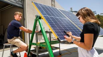 Two students run tests on solar panels in a Cal Poly engineering lab