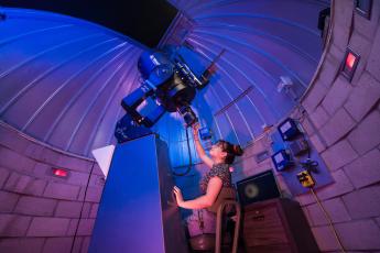 A woman sits and looks through a telescope at the Cal Poly Observatory.