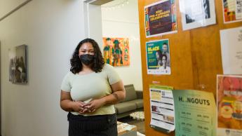 A person wearing a mask stands in an office doorway with colorful flyers on the back of an open door