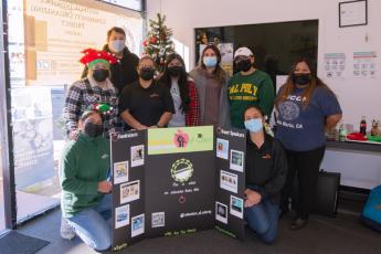 A group of masked students representing the Educators of Color club pose with a posterboard during a holiday book and gift drive.