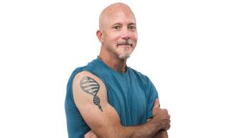 A man with rolled up sleeves displays a shoulder tattoo of a DNA double helix with the head of a snake