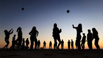 Students play with a volleyball at the sunset at the beach.