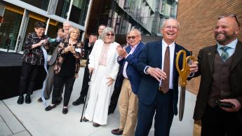 A group of people cuts a ribbon in front of the Frost Center with large scissors