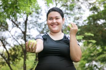A woman in a black shirt exercises while smiling and holding an apple