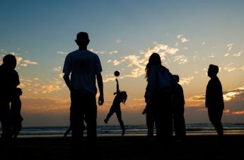 Students silhouetted against the sunset play ball during a bonfire at Grover Beach during Week of Welcome.