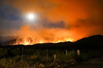 The sun shines through a cloud of orange smoke as a wildfire burns a California hillside
