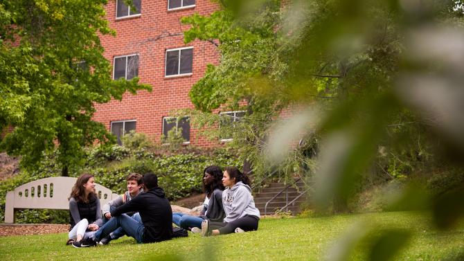 Students sitting on the lawn in front of the red brick dorms