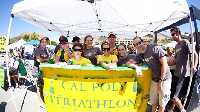 The Cal Poly Tri team smile as a group in their booth at Open House