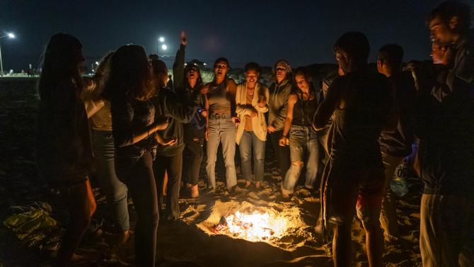 Students sitting around a bonfire at the beach at night