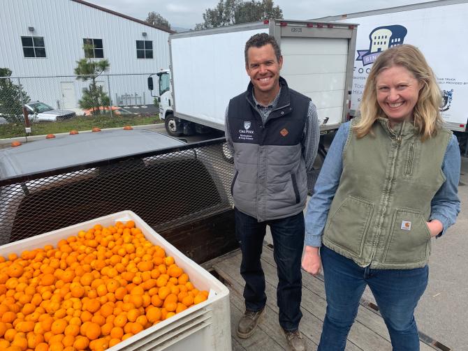 A man and a woman stand next to a large container of citrus set to be donated to SLO County residents in need. 