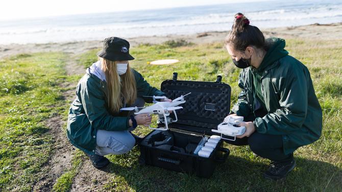 Two female students work with equipment on the bluffs by the ocean