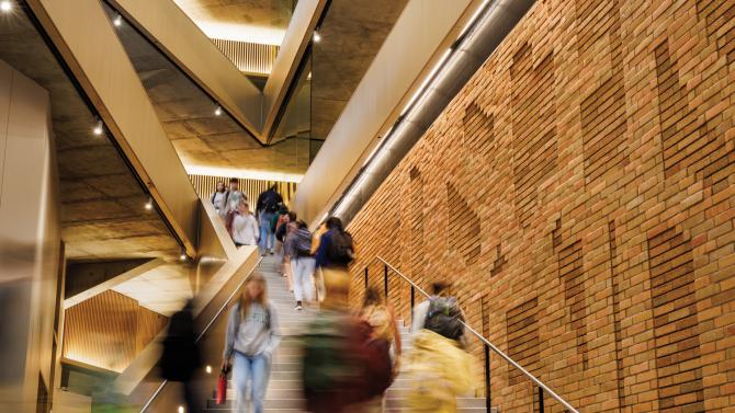Students walk on a staircase in the Frost Center next to a brick wall
