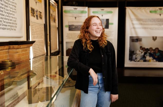 History student Jess O'Leary leans on a display case holding historical artifacts.