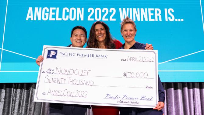 Three people stand on a stage holding an oversized $70,000 check