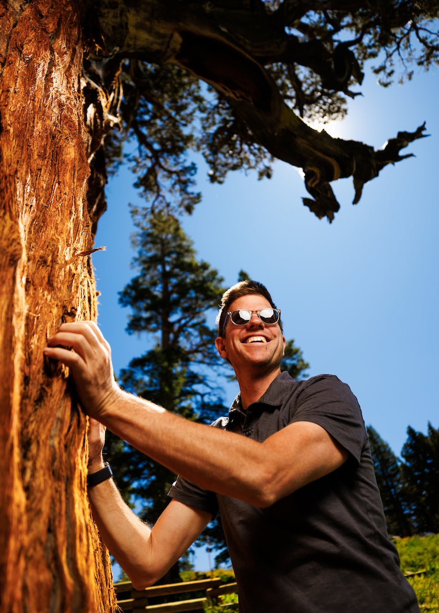 Matt Ritter smiles and poses with the Bennett Juniper during tree measuring.