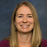 A professional headshot of a female professor with blonde hair, smiling.