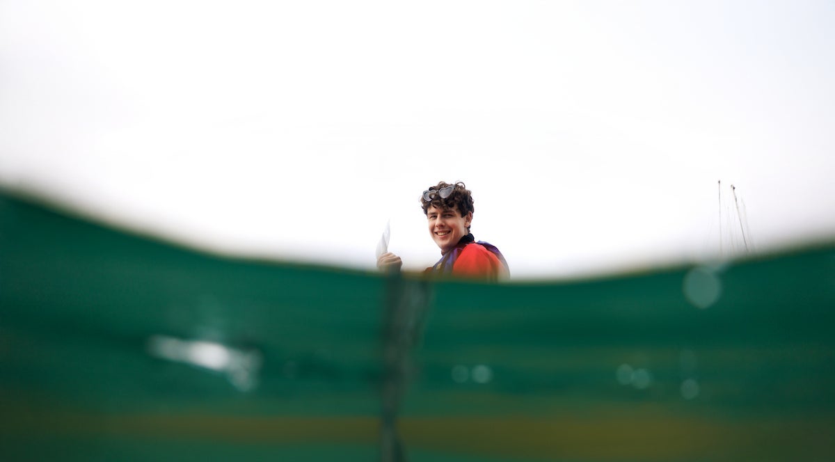 A student paddling in a kayak is seen looking up from the water.