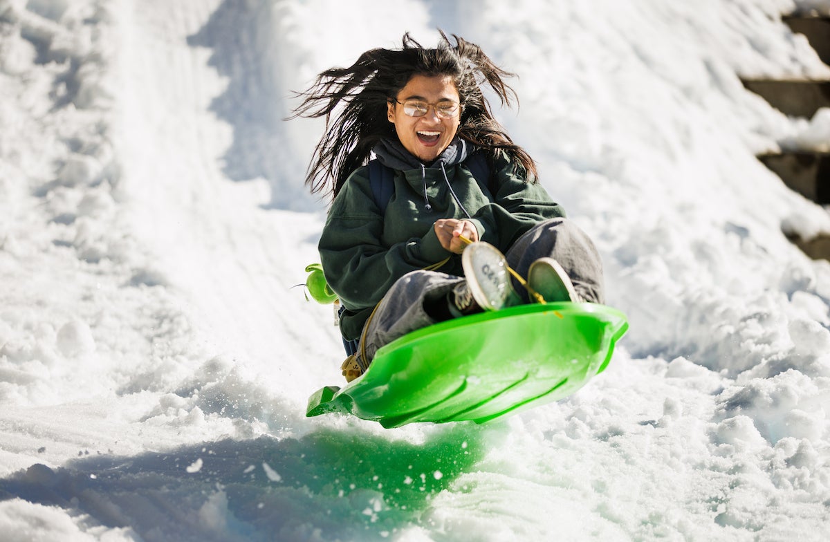 A student smiles as they ride a lime green sled down a mountain of shaved ice.