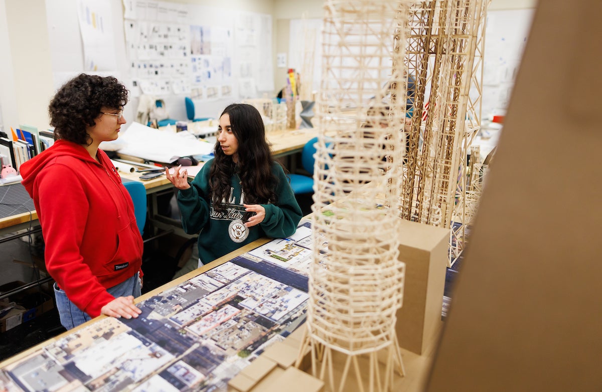 Students talk in the studio next to wooden scale models of skyscrapers.