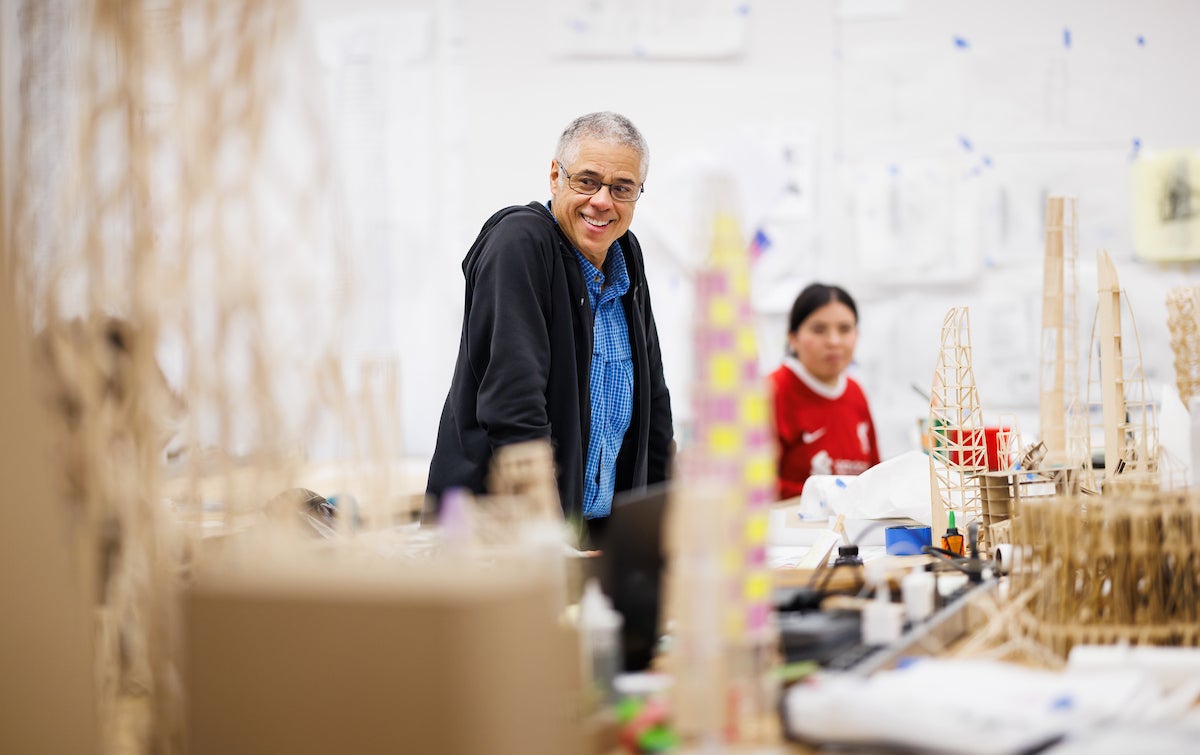 A professor stands and looks around at wooden scale models of skyscrapers.