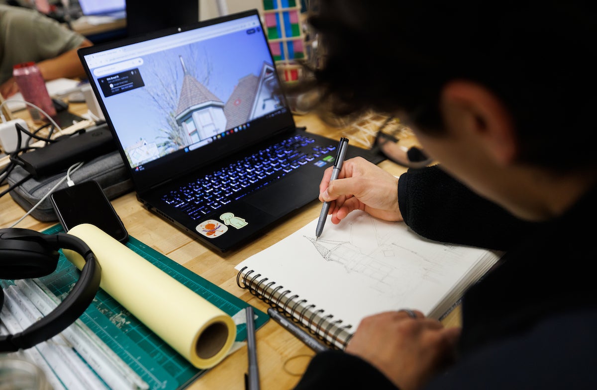 A student sketches a building in a notepad.