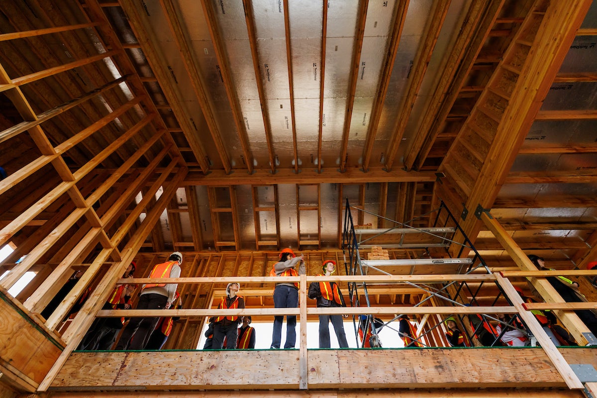 Students wearing orange vests and hard hats stand in a half-constructed buildling.