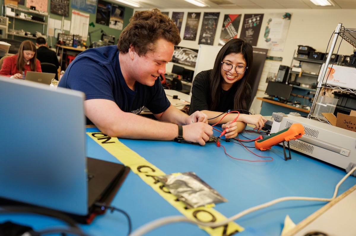 Students work on electrical equipment for a cubesat.