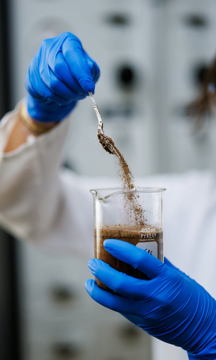 A detail image of a hand spooning soil into a beaker.