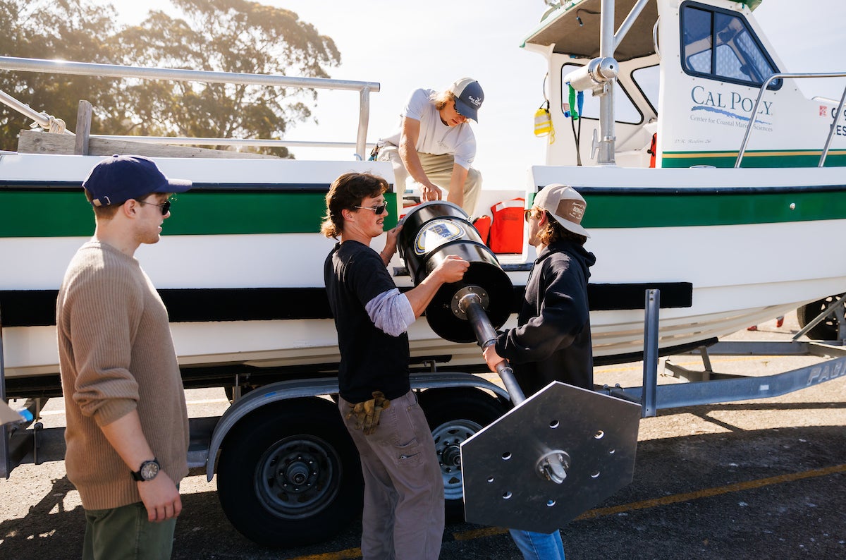 Students hoist their invention, an ocean powered generator, off of a boat in a parking lot close to Morro Bay.