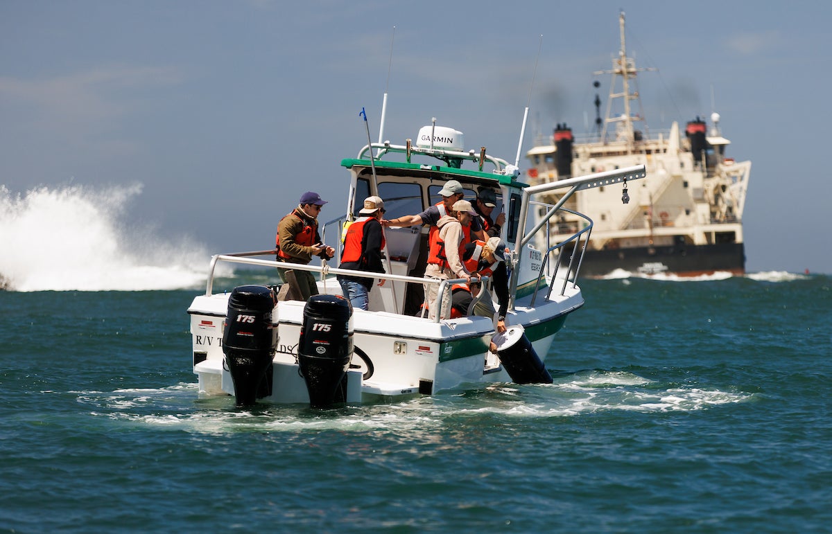 Students in a white research vessel drop an ocean powered generator into the waters of Morro Bay.