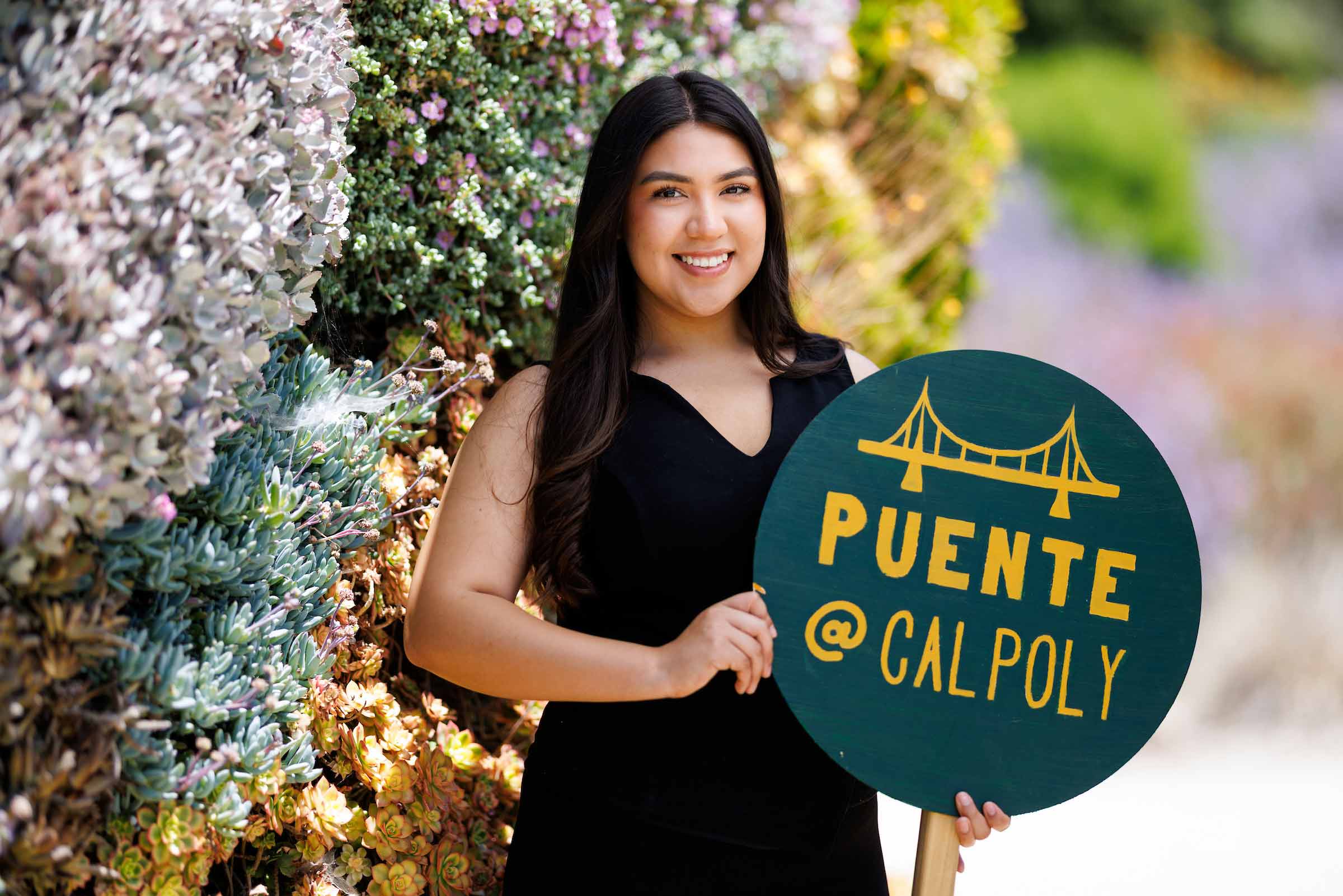 Denis Gonzalez-Reyes holds a green circular sign that says Puente @ Cal Poly