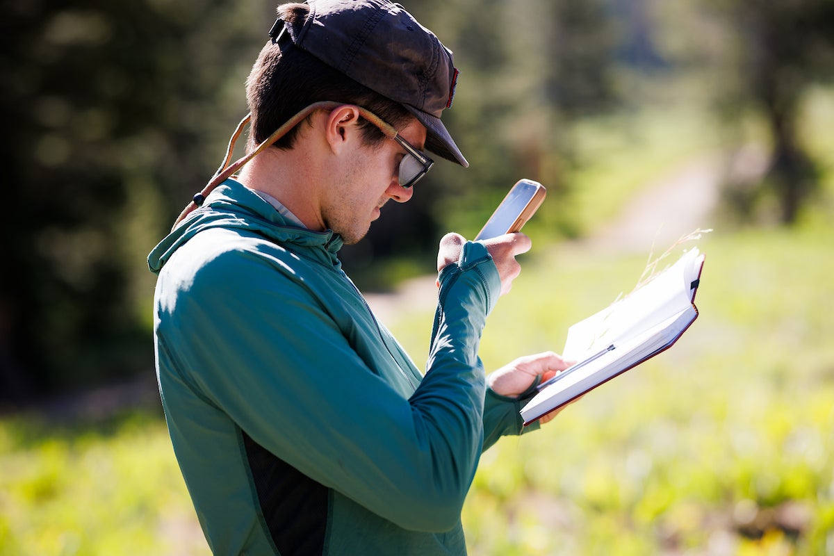 A student holds a notebook in one hand and a phone in another.