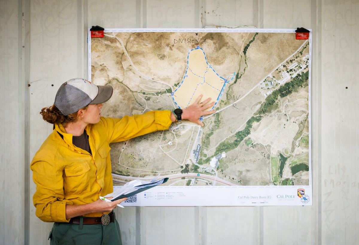 A woman in firefighting gear points at a map.