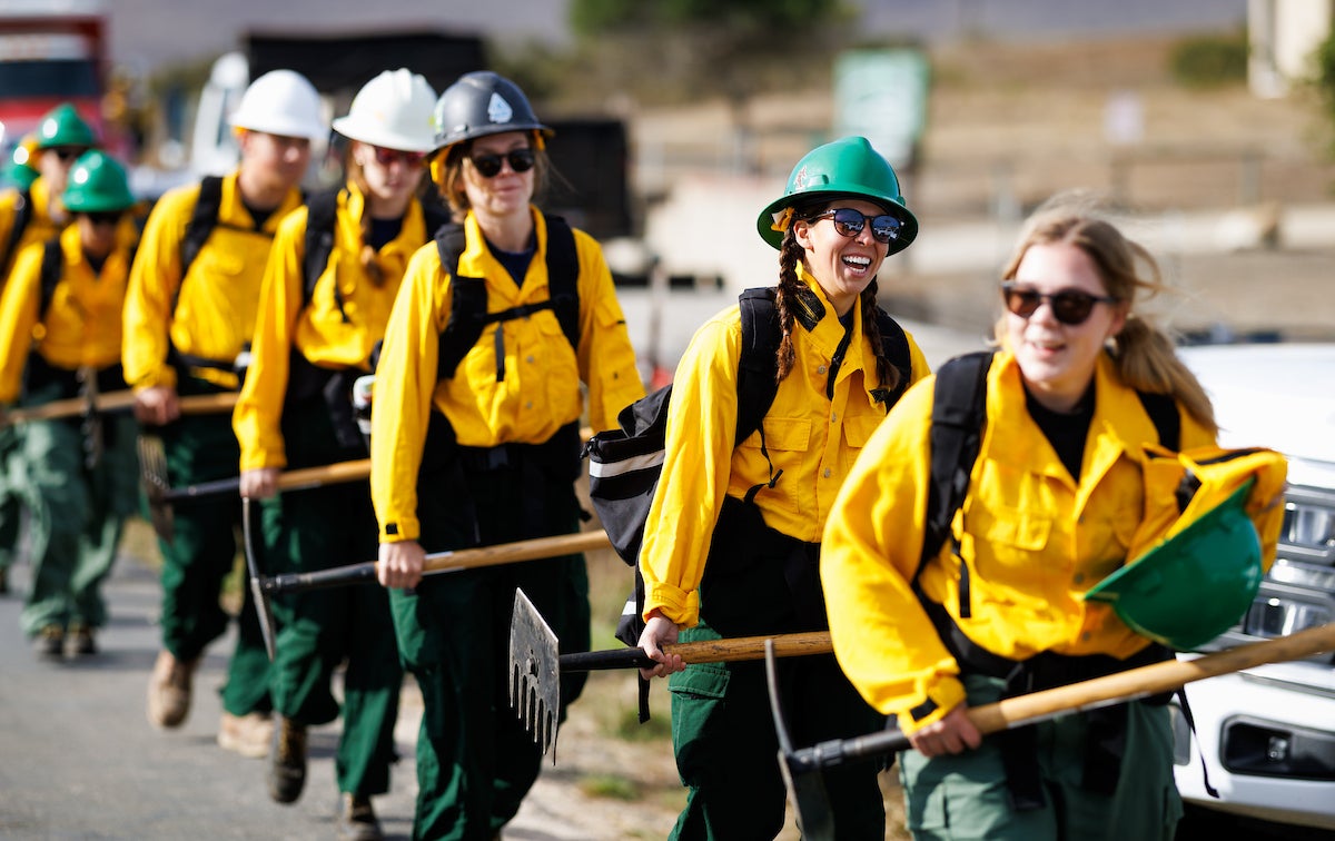 A line of Cal Poly students walk and carry firefighting tools.