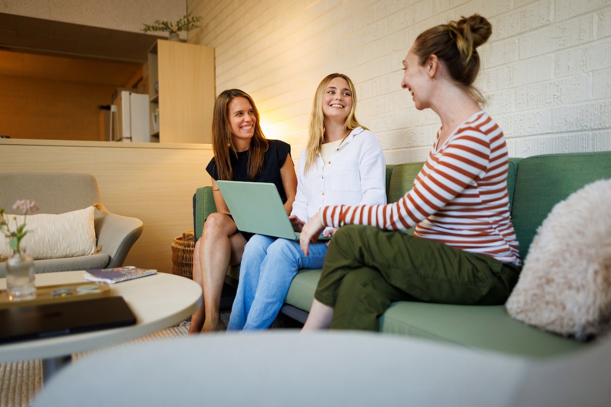 Two staff members and a student smile and talk on a couch.