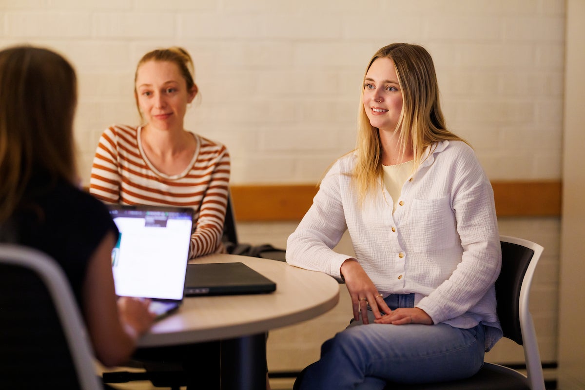 A student sits at a table with two other people.
