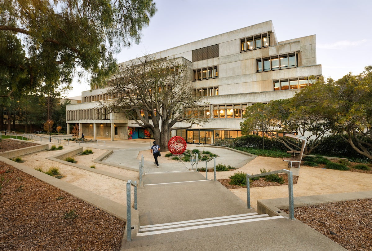 A view of Kennedy Library at dusk. A student is walking down the concrete steps toward the building.