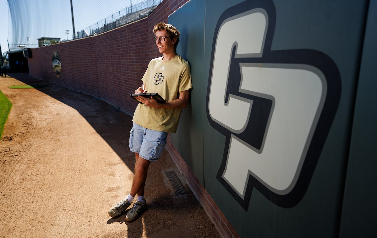 Gabe Riedel leans against a Cal Poly-branded wall at the baseball stadium.