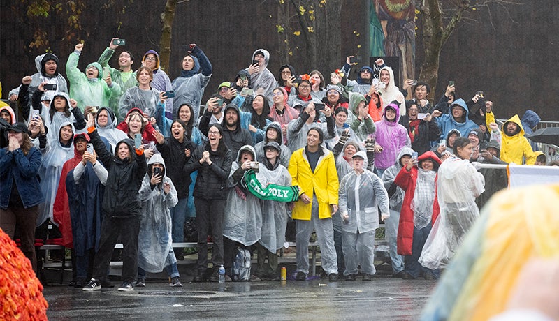 Students wearing ponchos and holding Cal Poly gear cheer on the sidelines.