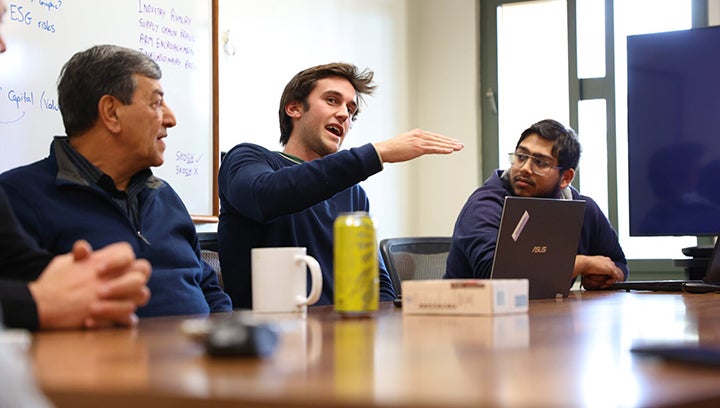 Benjamin Roe discusses his team’s analysis with visiting alumni and Finance chair Cyrus Ramezani, left. To his right is team member Jivitesh Kamboj. (Photo: Pat Pemberton)