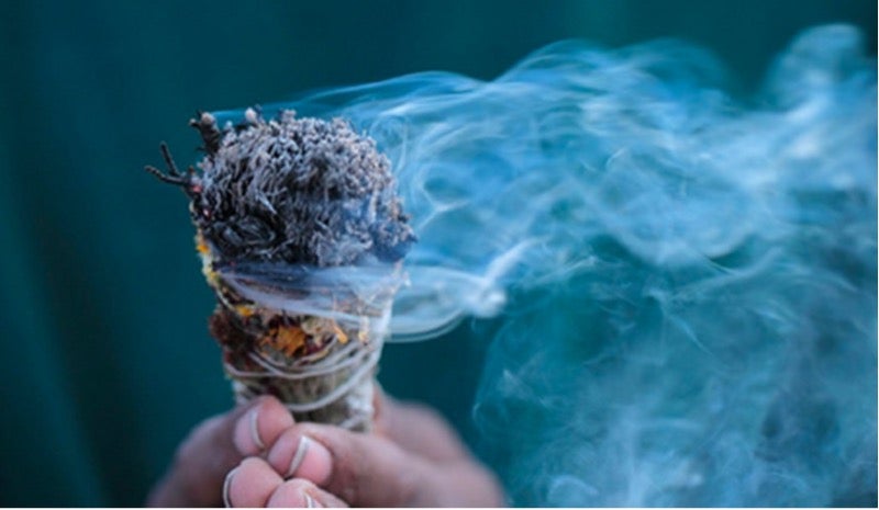 A hand holds a smoking bundle of white sage.