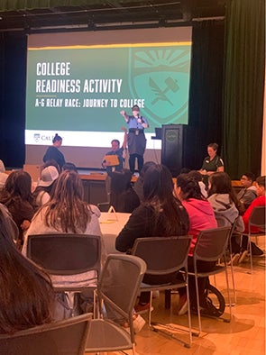 Middle school students sit and listen to a presentation while facing a screen reading "College Readiness Activity."
